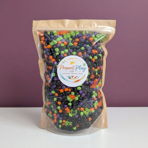 Halloween sensory mix in its original Present Play Co. pouch against a muted plum backdrop with a white tabletop
